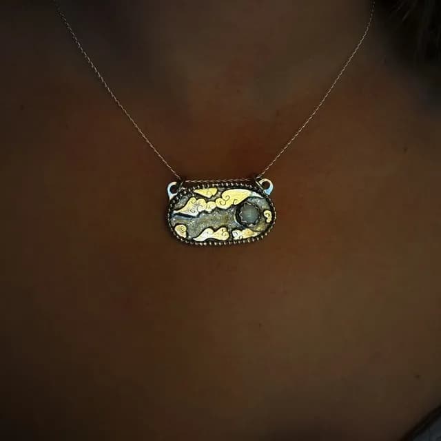 Médaillon ovale en argent gravé de nuages et d'une lune en opale, suspendu sur un support en bronze.