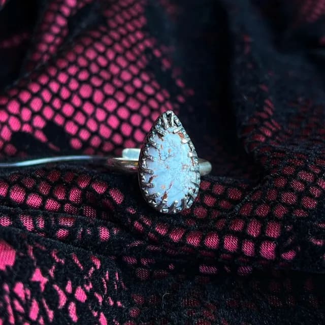 Bague en argent avec une pierre en forme de goutte blanche et brune, posée sur de la dentelle noire et rose.