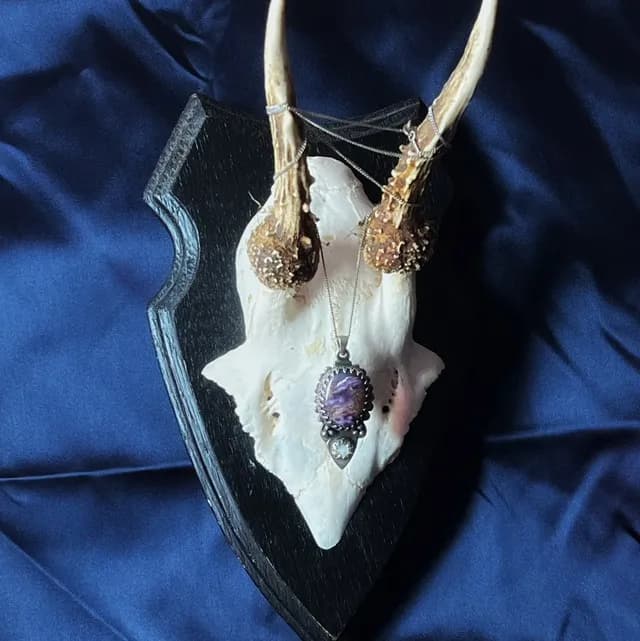 Pendentif Éclipse en argent et pierres violette et blanche suspendu à un crâne sur fond bleu satiné.