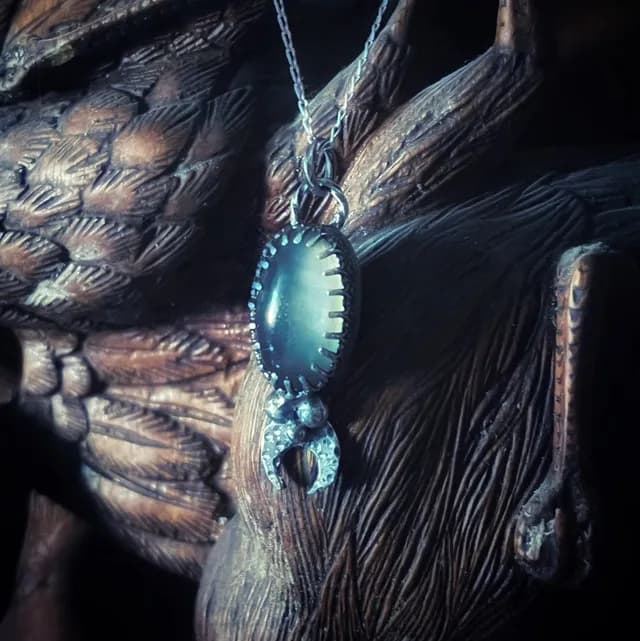 Pendentif en argent avec obsidienne grise et croissant de lune, posé sur une sculpture en bois.