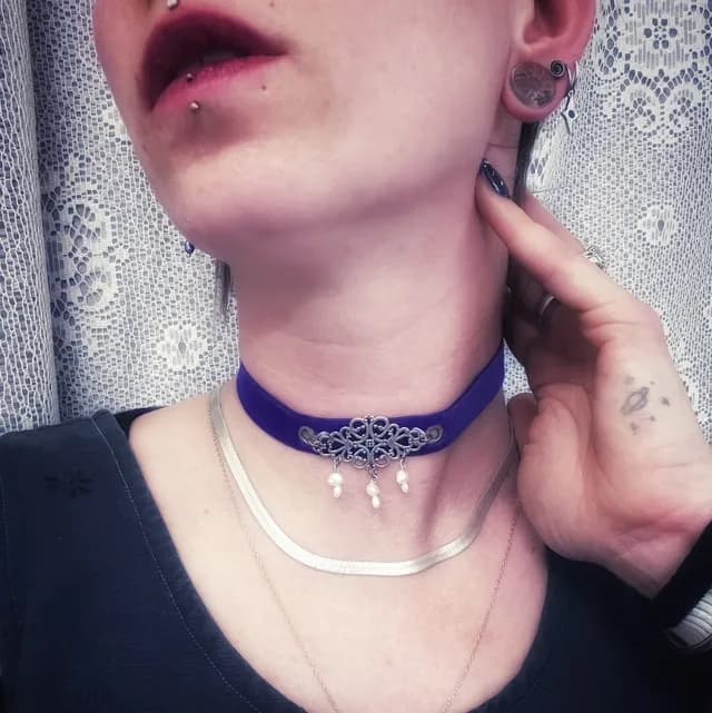 Collier ras de cou en velours violet avec ornement en métal argenté et perles blanches, porté.