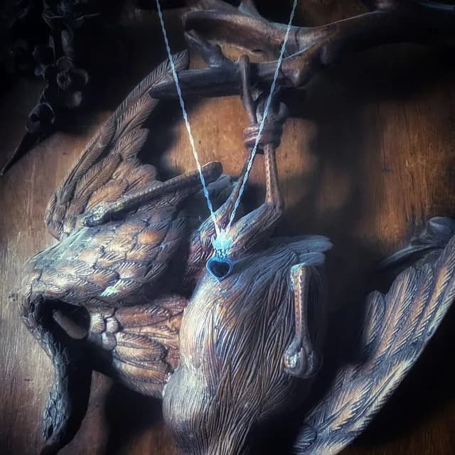 Collier avec pendentif cœur noir et flamme argentée suspendu devant une sculpture d'oiseau en bois.