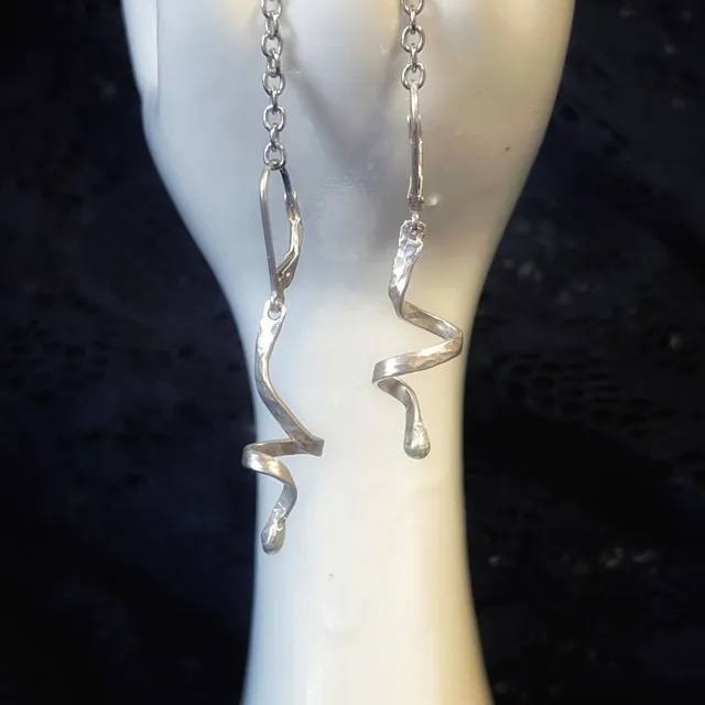 Gros plan de boucles d'oreilles argentées en spirale suspendues sur un support en forme de main blanche.