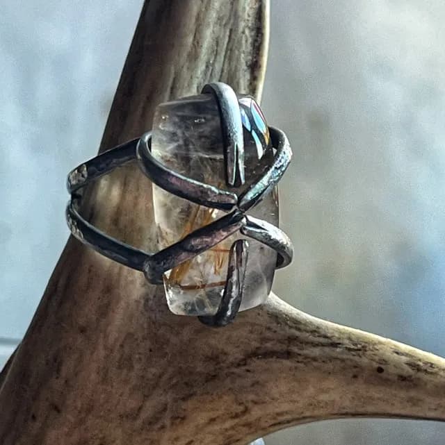 Gros plan de la bague en argent texturé enserrant un quartz rutile transparent, posée sur un support en corne.