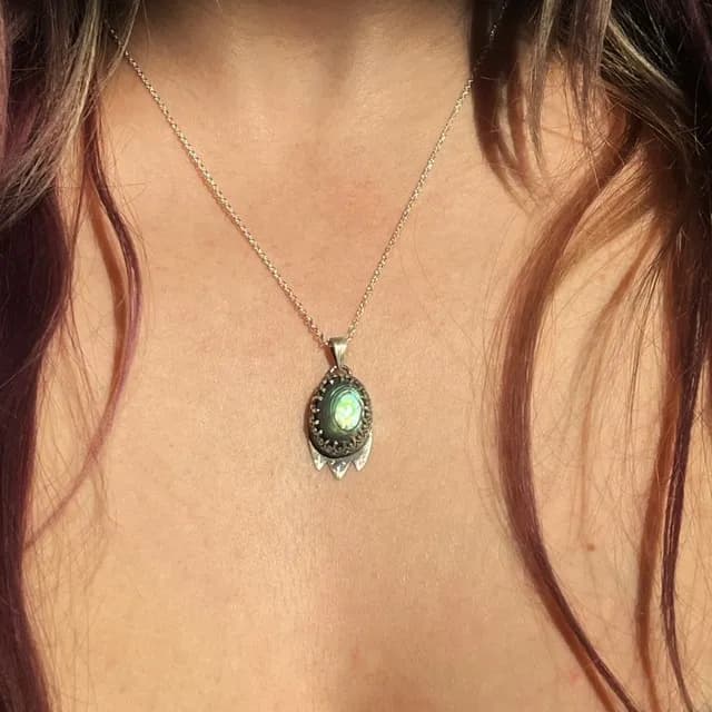 Pendentif en argent avec cabochon d'abalone vert et bleu, porté sur le décolleté.