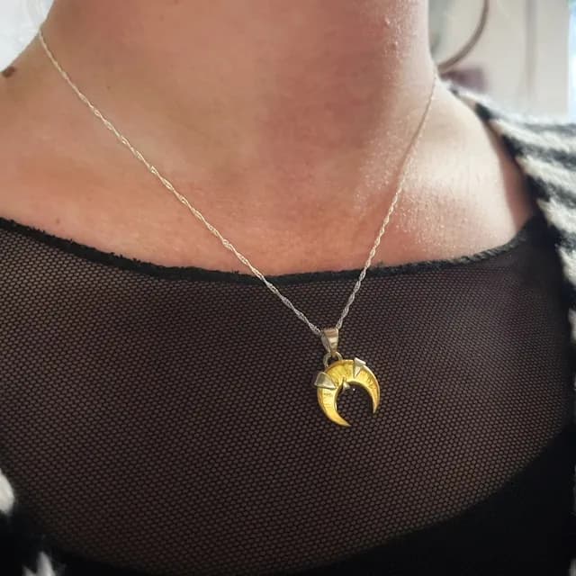 Collier avec pendentif en forme de croissant de lune doré et argenté, porté sur le décolleté.