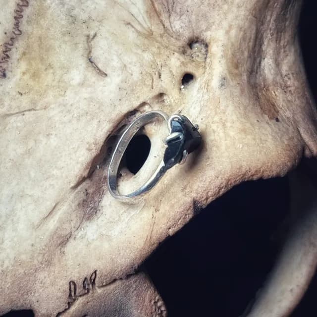 Bague en argent avec pierre brute noire posée sur un support en os texturé.