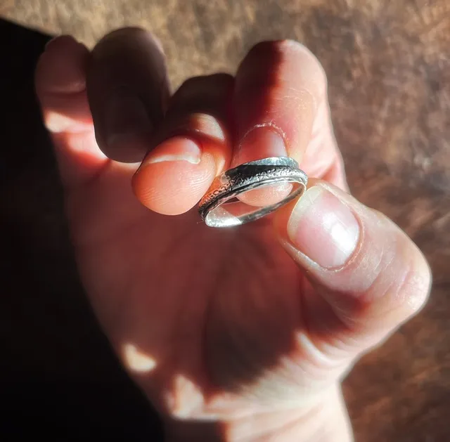 Bague en argent martelé avec anneau mobile gravé, tenue entre les doigts d'une main.