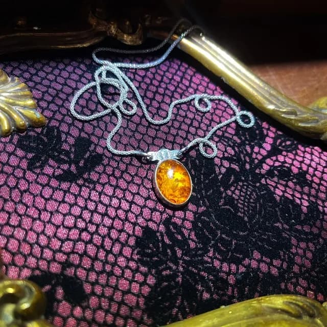 Collier en argent avec pendentif d'ambre jaune posé sur une dentelle rose et noire dans un cadre doré.