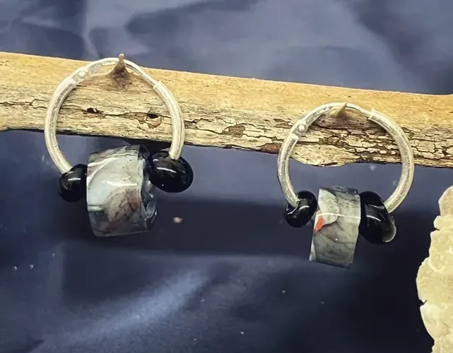 Paire de créoles en argent avec perles de verre grises et noires, posées sur une branche en bois.