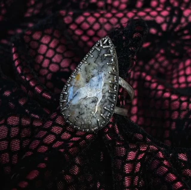 Bague en argent avec une agate dendrite en forme de goutte, posée sur une dentelle noire et rose.