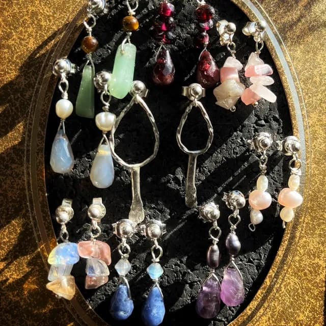 Plusieurs paires de boucles d'oreilles artisanales colorées présentées sur un support noir ovale.
