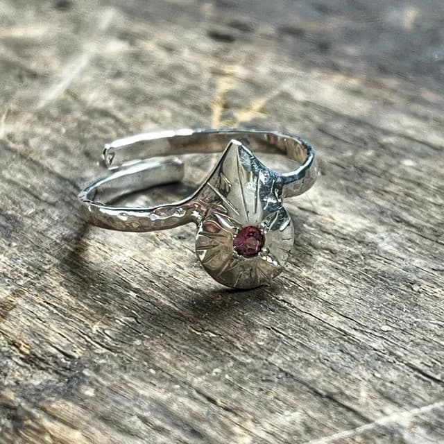 Bague en argent martelé avec un motif de goutte gravé et une pierre rose centrale, posée sur du bois.