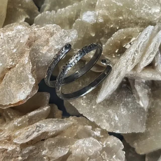 Bague de phalange en argent texturé en forme de spirale posée sur des cristaux beiges.