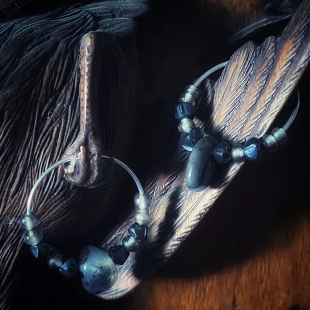 Créoles en argent avec perles d'agate grise et perles de verre sombres sur une sculpture en bois.