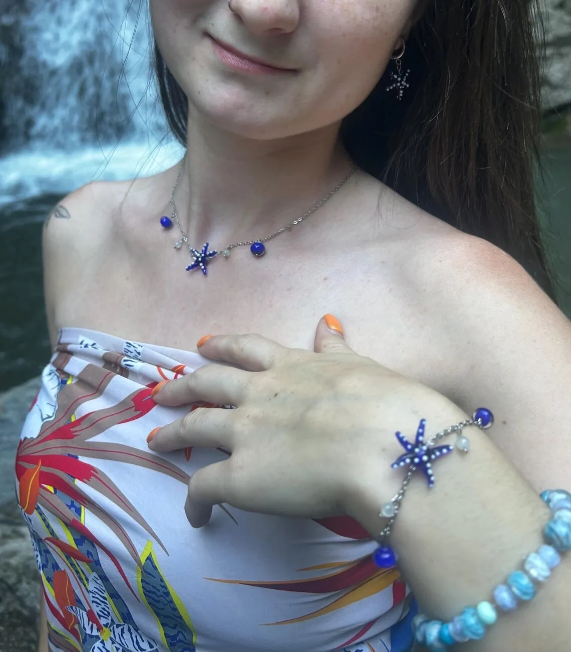Femme portant un bracelet et un collier assortis avec une étoile de mer bleue, devant une cascade.