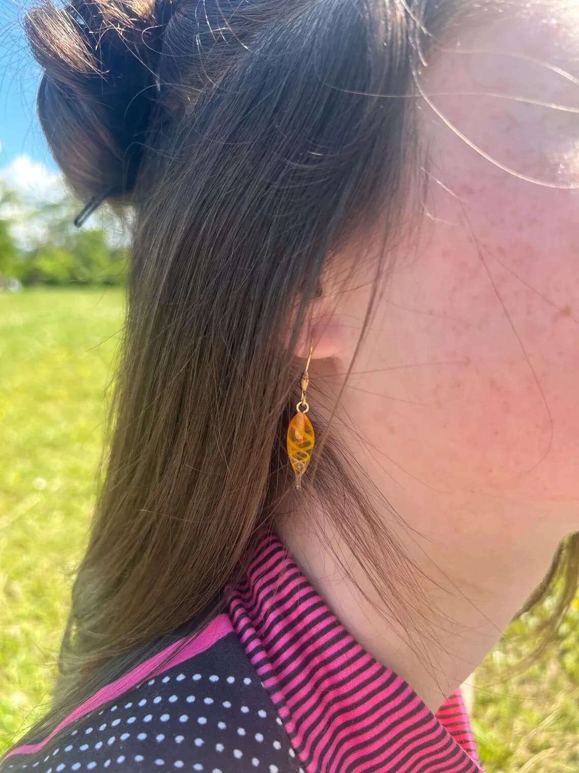 Paire de boucles d'oreilles gouttes orange ambré suspendues sur un support blanc devant l'eau.