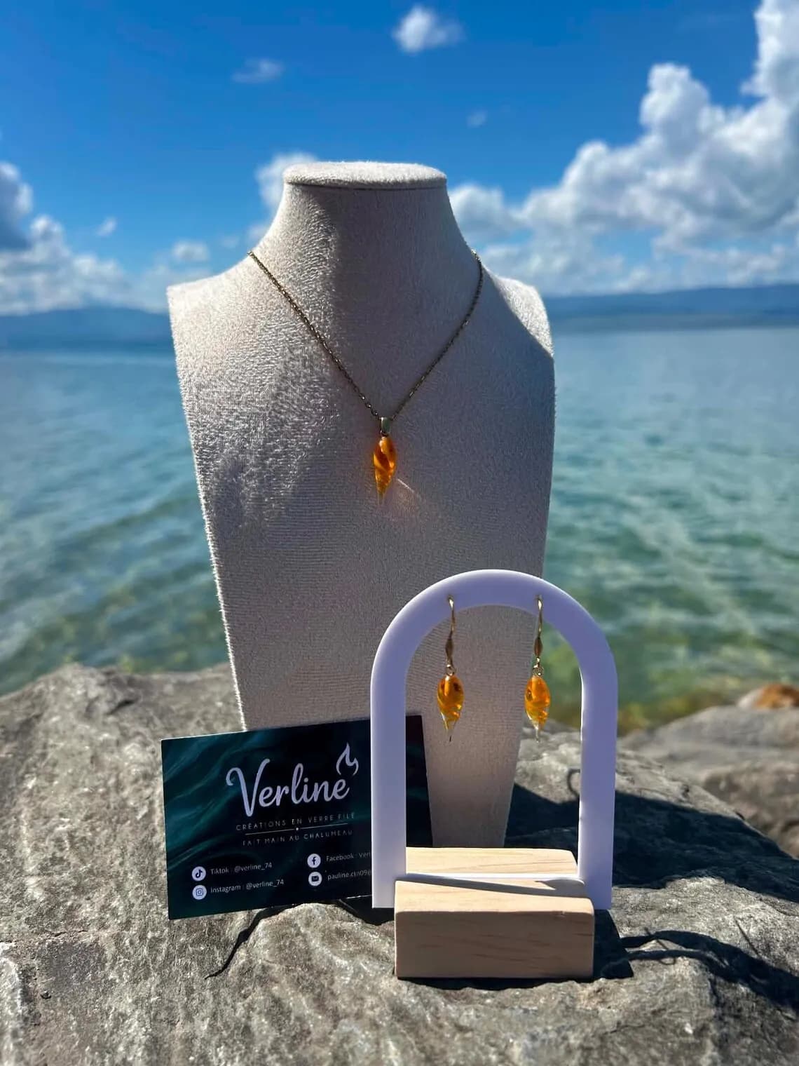 Collier et boucles d'oreilles orange en forme de goutte présentés sur un rocher face à un lac bleu.