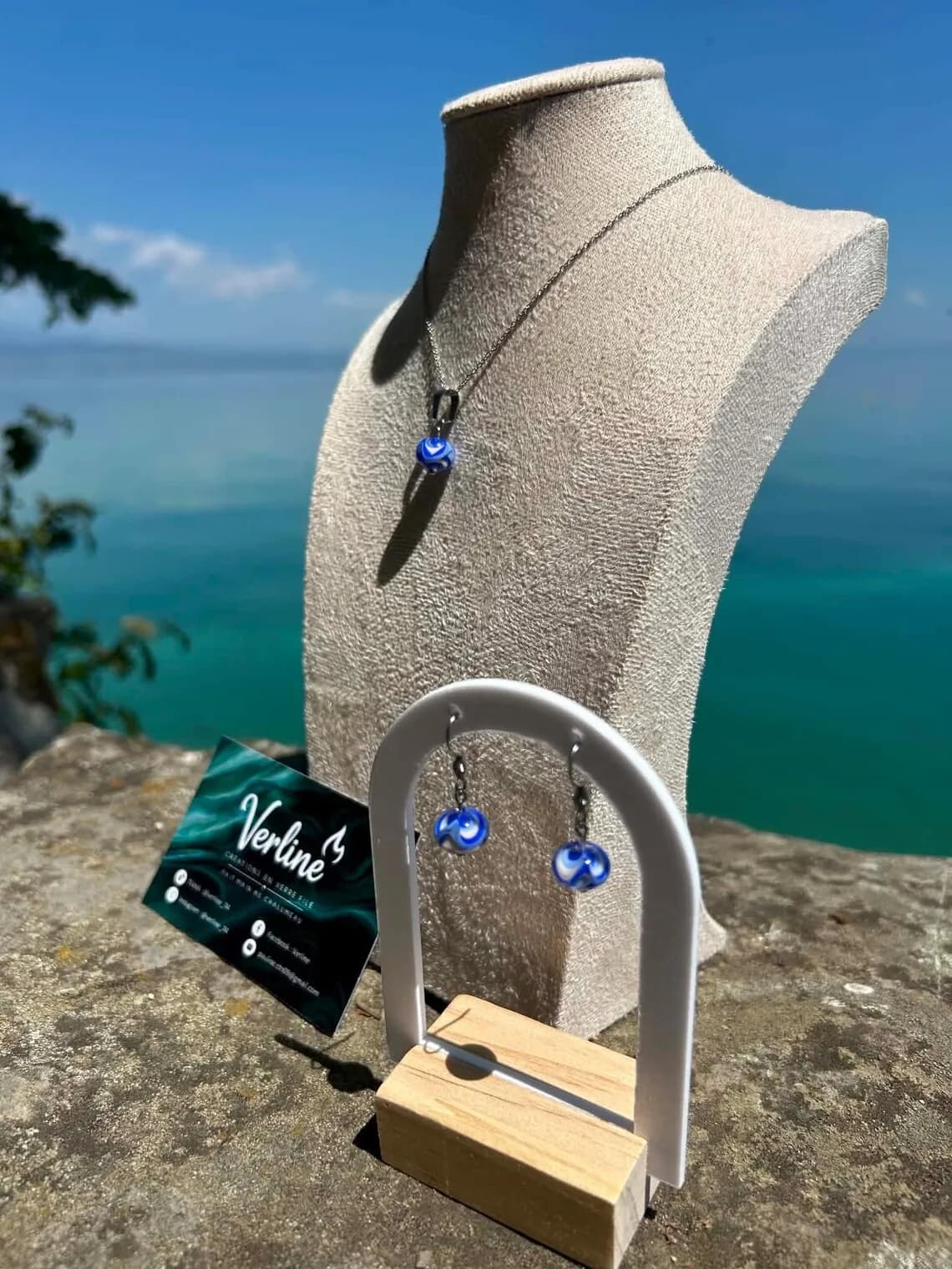 Coffret de bijoux avec collier et boucles d'oreilles bleus et blancs présentés face à la mer.