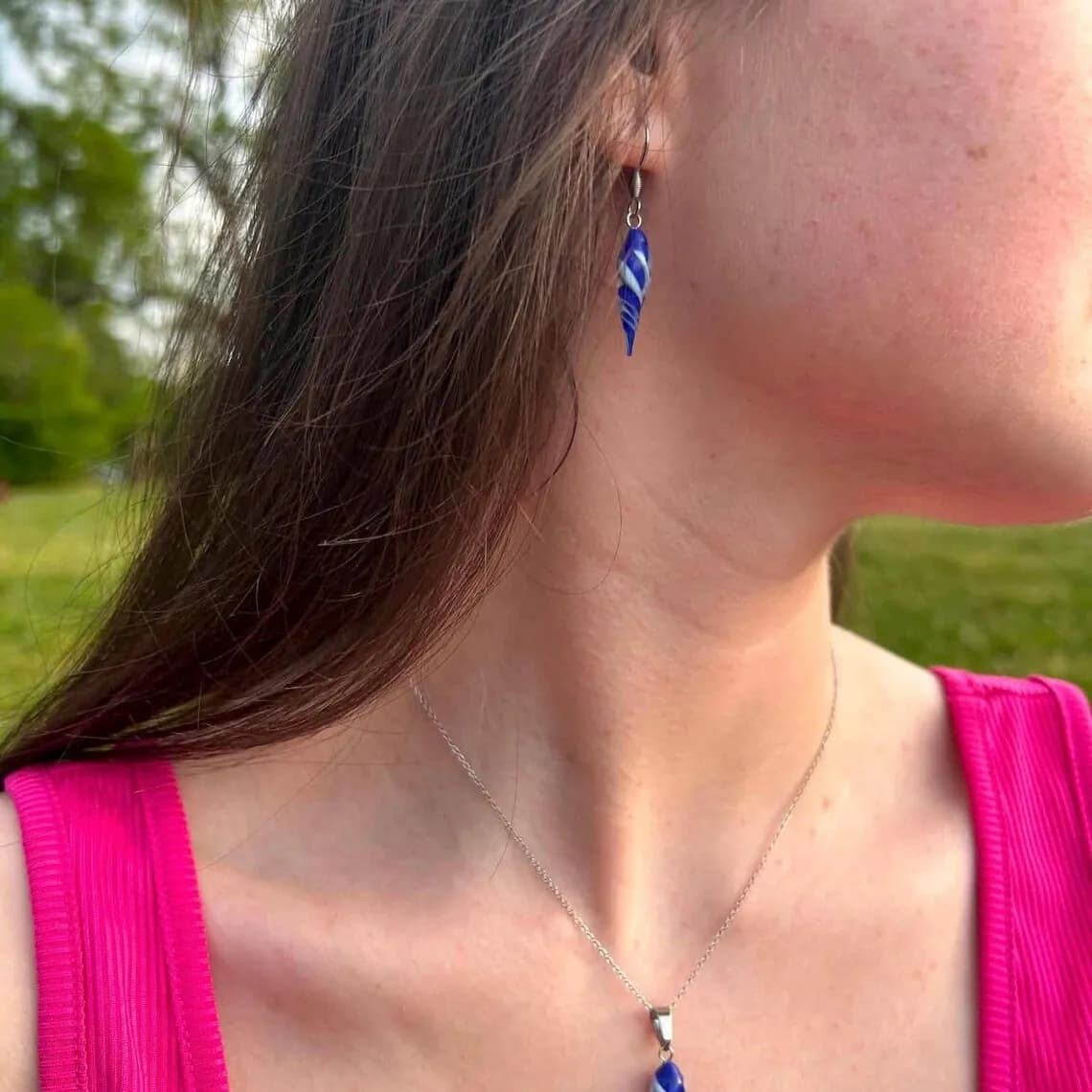 Boucle d'oreille pendante bleue et blanche en forme de goutte torsadée, portée par une femme.