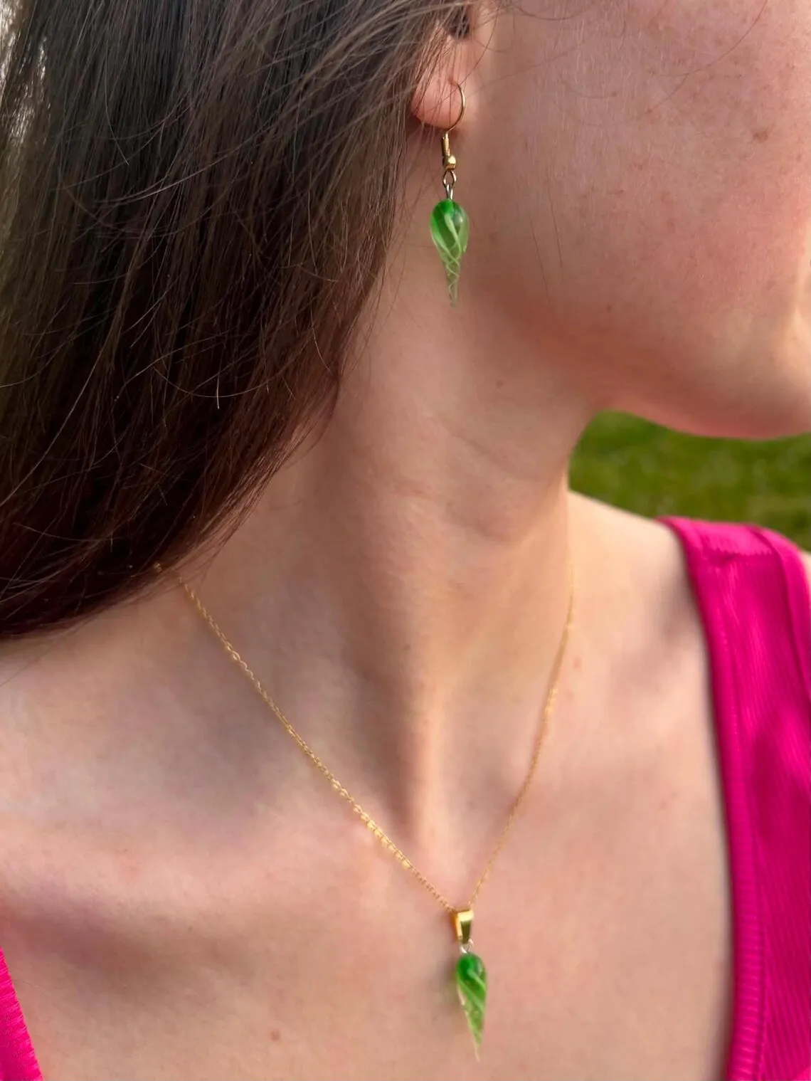 Boucle d'oreille pendante et collier assorti en verre vert torsadé, portés par une femme de profil.