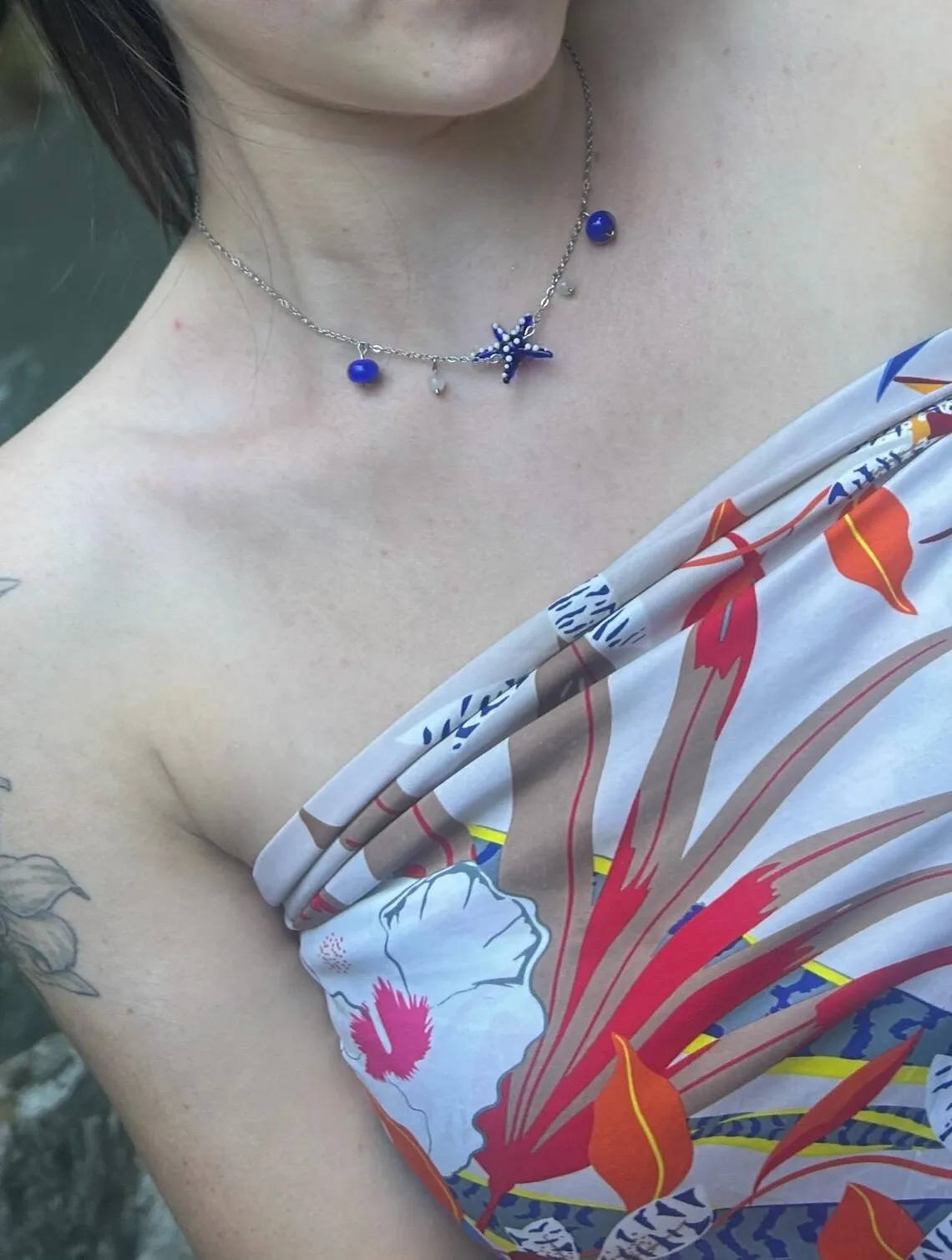 Collier et bracelet assortis avec étoile de mer bleue, portés par une femme devant une cascade.