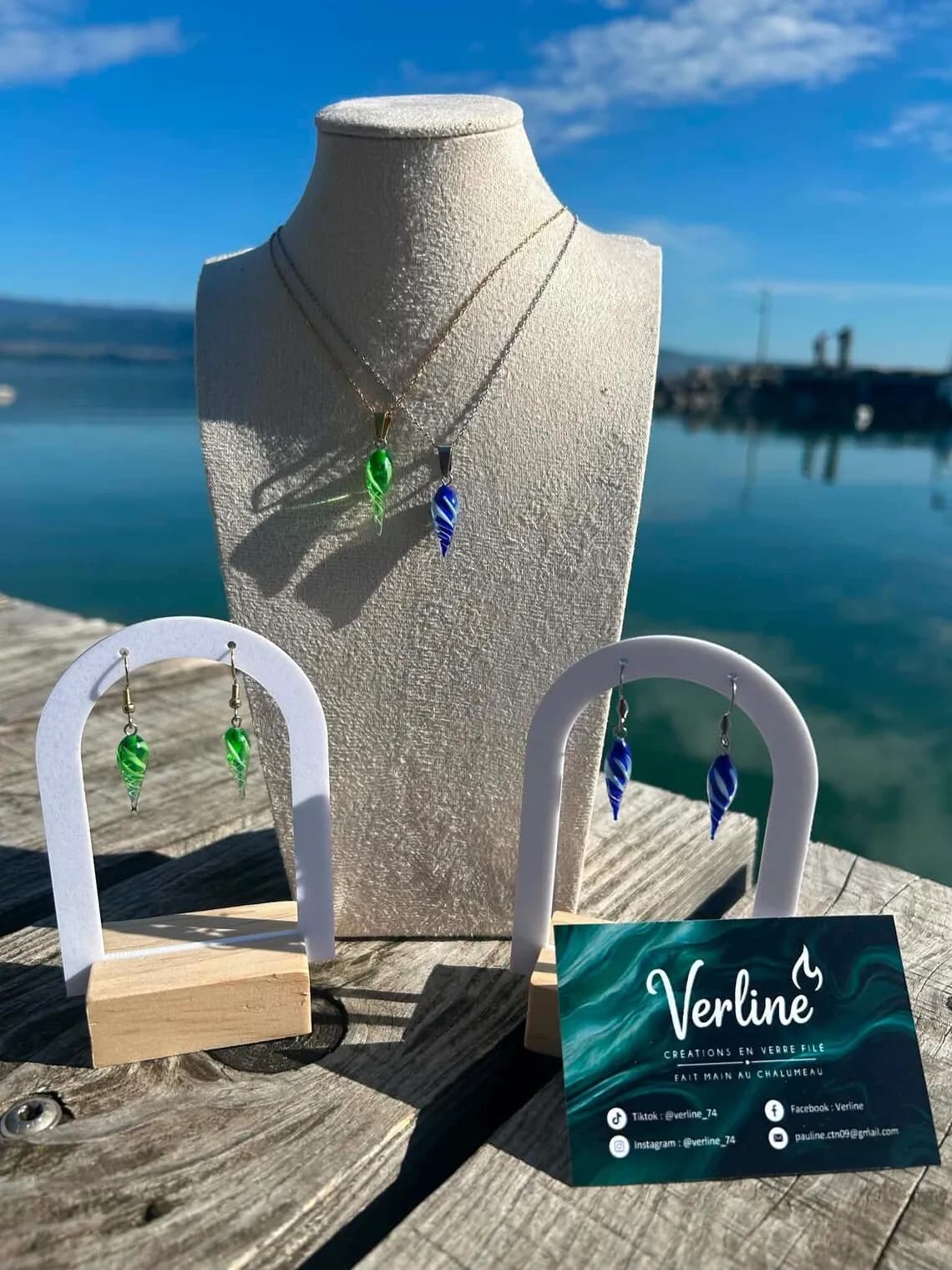 Colliers et boucles d'oreilles en forme de gouttes vertes et bleues, présentés en extérieur face à un lac.