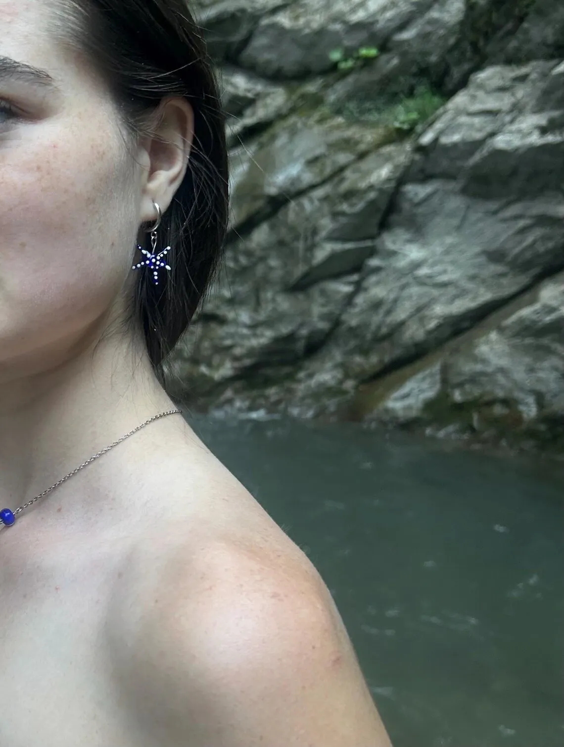 Boucle d'oreille étoile de mer bleue portée, avec un fond de rivière et de rochers.