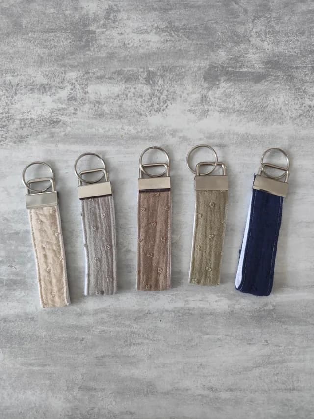 Alignement de cinq porte-clés en tissu texturé à pois de différentes couleurs neutres et bleu marine