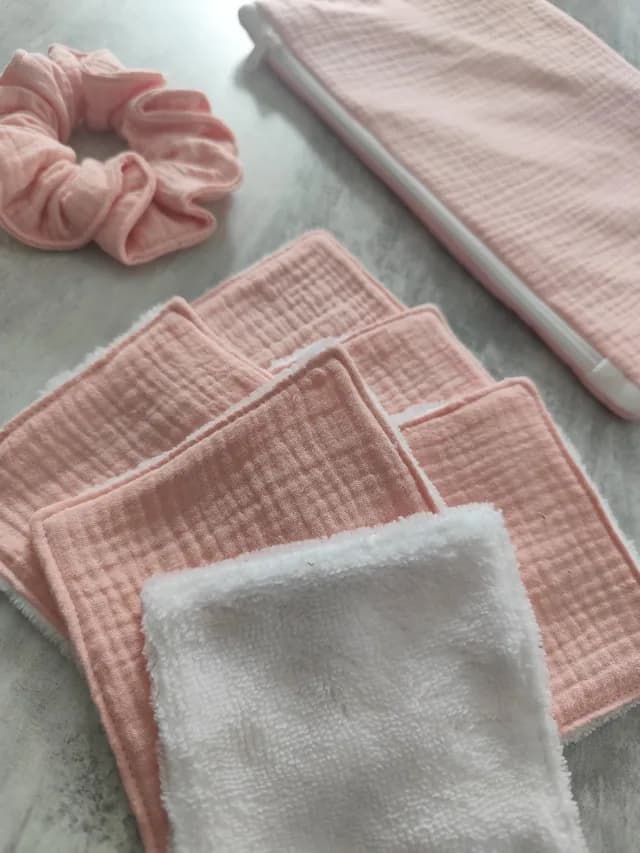 Gros plan sur les lingettes lavables roses et blanche, le chouchou et la pochette en arrière-plan