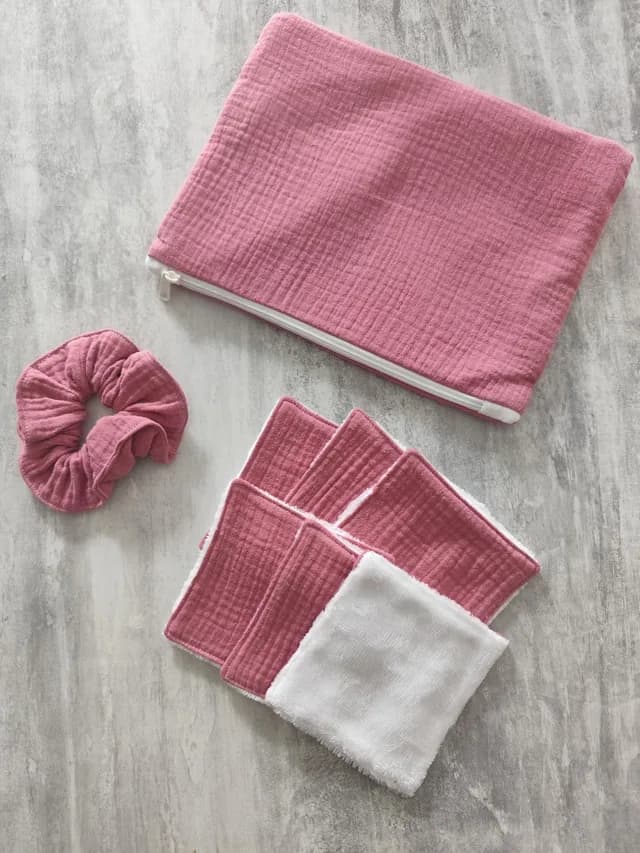 Kit pochette zippée, chouchou et lingettes lavables roses et blanches disposés sur fond gris effet béton