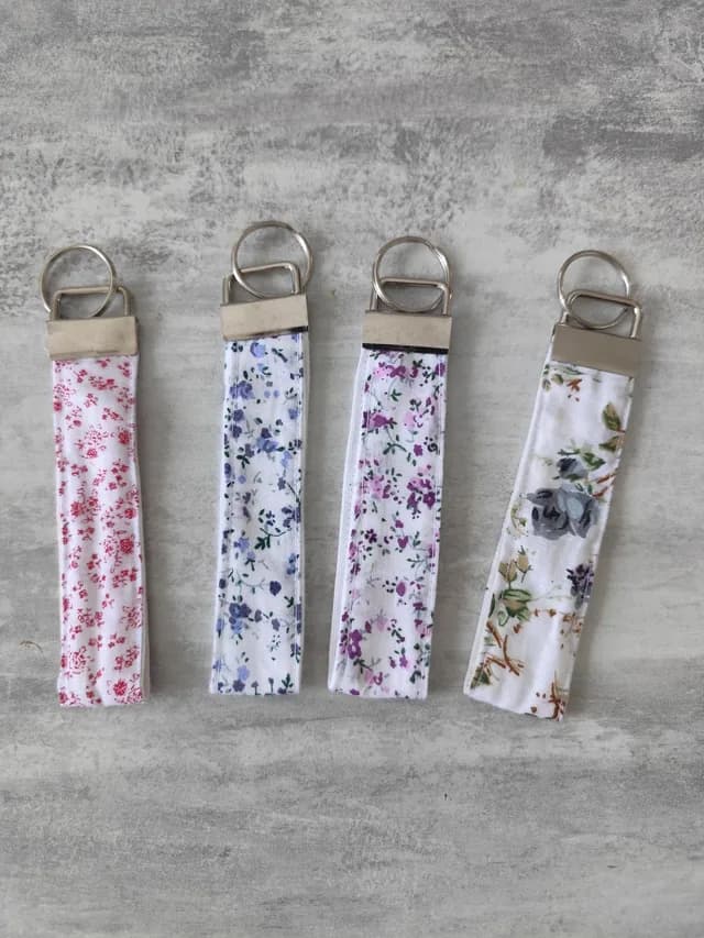 Quatre porte-clés rubans en tissu à motifs floraux rouge, bleu, violet et beige alignés.