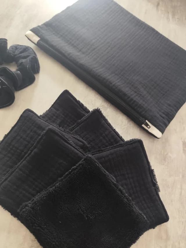 Gros plan en angle sur des lingettes lavables noires, une pochette et un chouchou textile assortis.