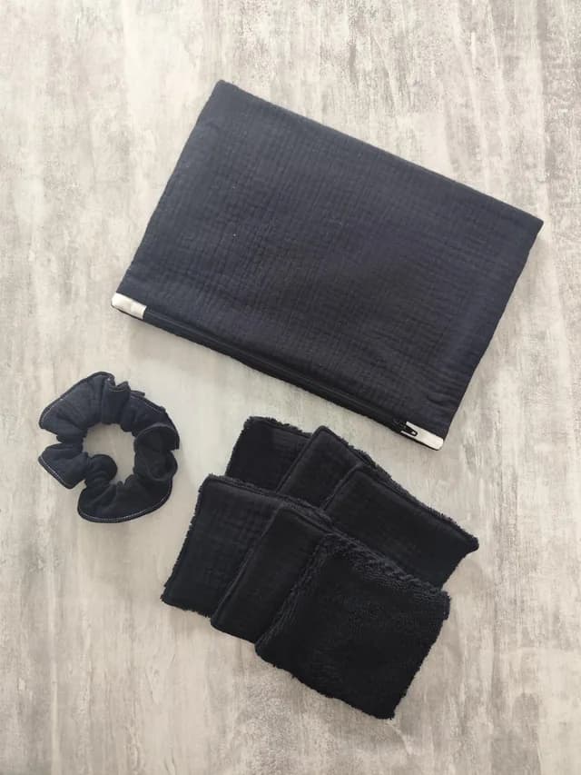 Vue de dessus d'un kit textile noir comprenant une pochette zippée, six lingettes lavables et un chouchou.